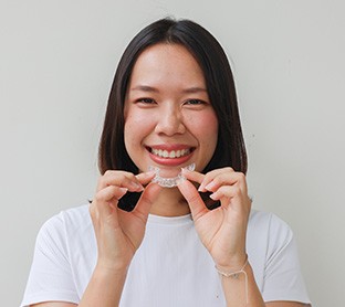 Woman smiling while holding Invisalign aligner