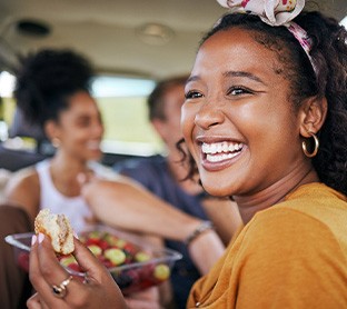 Woman smiling while eating lunch in car with friends