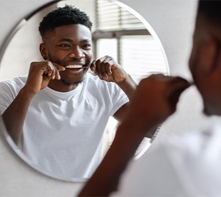 Man smiling while flossing his teeth in bathroom